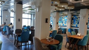 Un restaurante con mesas y sillas redondas, pilares grandes y un techo con iluminación empotrada.