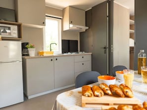 Eine moderne Küche mit Kühlschrank, Herd und Schränken. Ein Esstisch mit Schneidebrett und Lebensmitteln steht bereit.