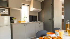 Een moderne keuken met een koelkast, fornuis en kasten. Er staat een eettafel met een snijplank en etenswaren.