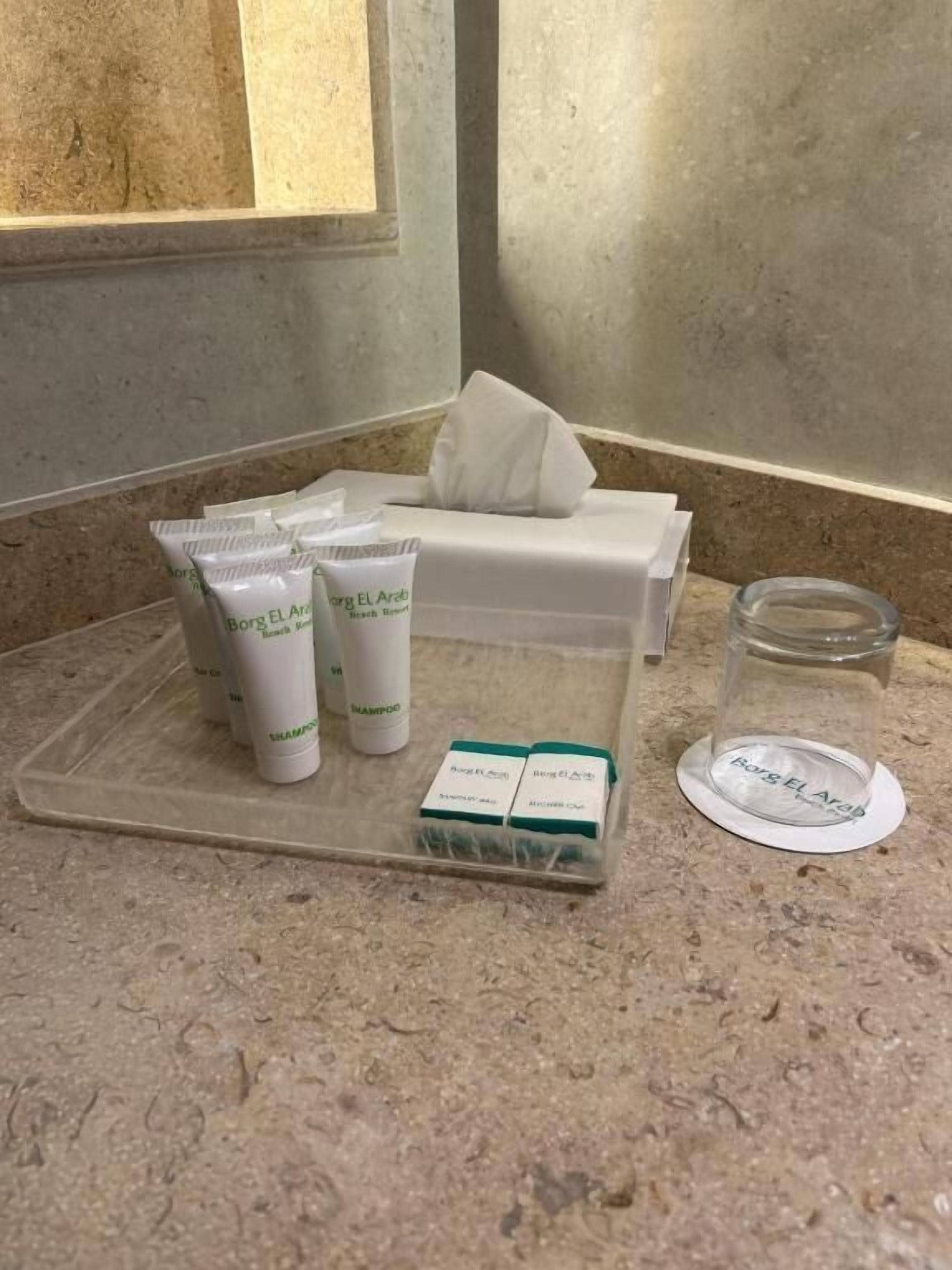 Un mostrador de baño con artículos de aseo, incluyendo champú, acondicionador y un vaso de agua.
