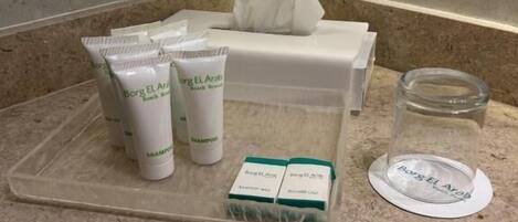 Un mostrador de baño con artículos de aseo, incluyendo champú, acondicionador y un vaso de agua.