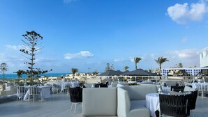 An outdoor seating area with tables and chairs, a sofa, and a view of the sea.