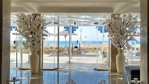 A modern lobby with a glass entrance, two large white vases, and a view of the beach.