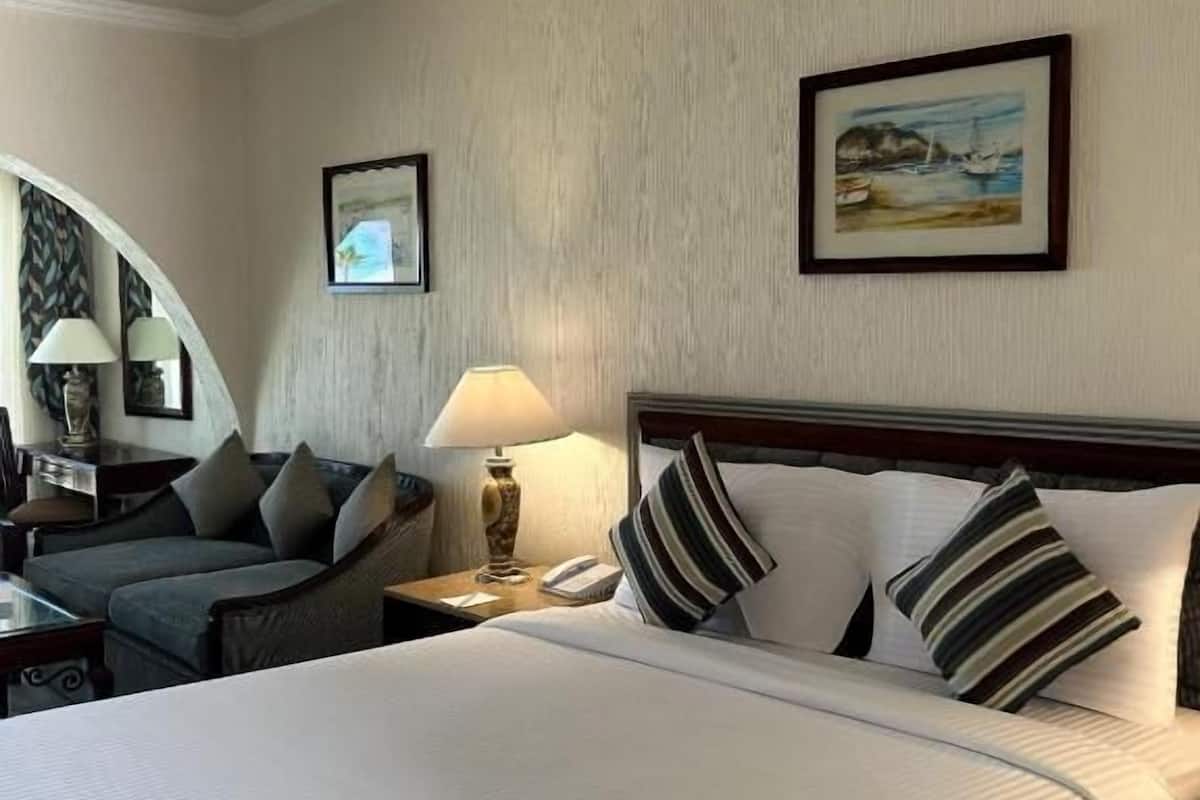 A hotel room with a large bed, a desk with a lamp, two chairs, a nightstand, and two framed pictures on the wall.