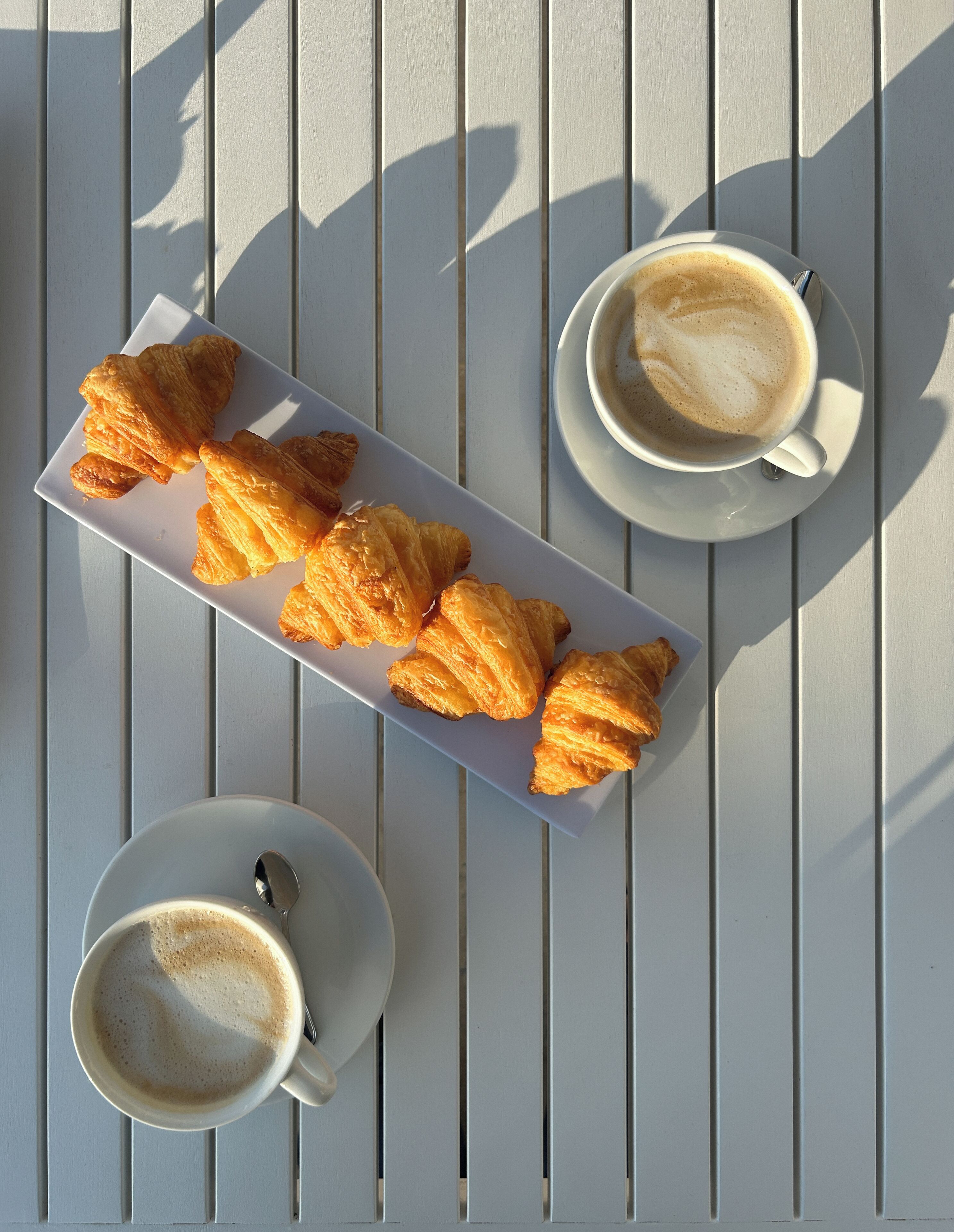 Une table blanche avec une assiette de croissants et deux tasses de café.