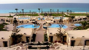 A resort with multiple swimming pools, palm trees, and a beach view.