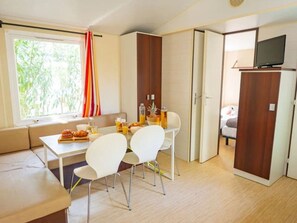 Ein gemütlicher Raum mit Esstisch, Stühlen, einer Couch, einem Fernseher und einem Kleiderschrank.