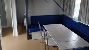 Una habitación con una mesa, sillas, un banco, una ventana con cortinas y una puerta.