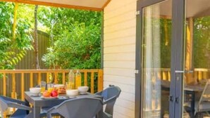 Un patio techado con una mesa y sillas, una terraza de madera y un ventanal que da a una habitación.
