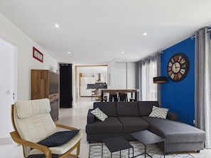Ein modernes Wohnzimmer mit Sofa, Sessel und Couchtisch, ein Essbereich mit Tisch und Stühlen sowie eine Küche im Hintergrund.