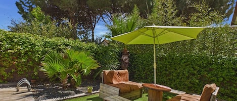 Una terraza de madera con zona de césped artificial verde, rodeada de abundante vegetación y árboles.