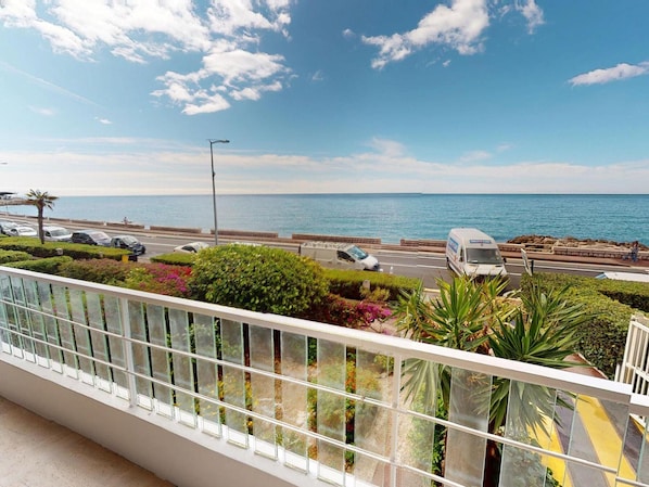 A balcony with a view of the sea, a road with parked cars, and a van. - Pleasant apartment sea view - 4 guests (Menton)