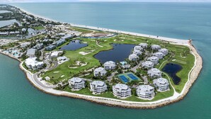 An aerial view of a coastal resort with multiple buildings, a golf course, and a beach.