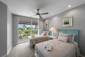 A hotel room with two beds, a ceiling fan, a balcony with a view, and a painting on the wall.