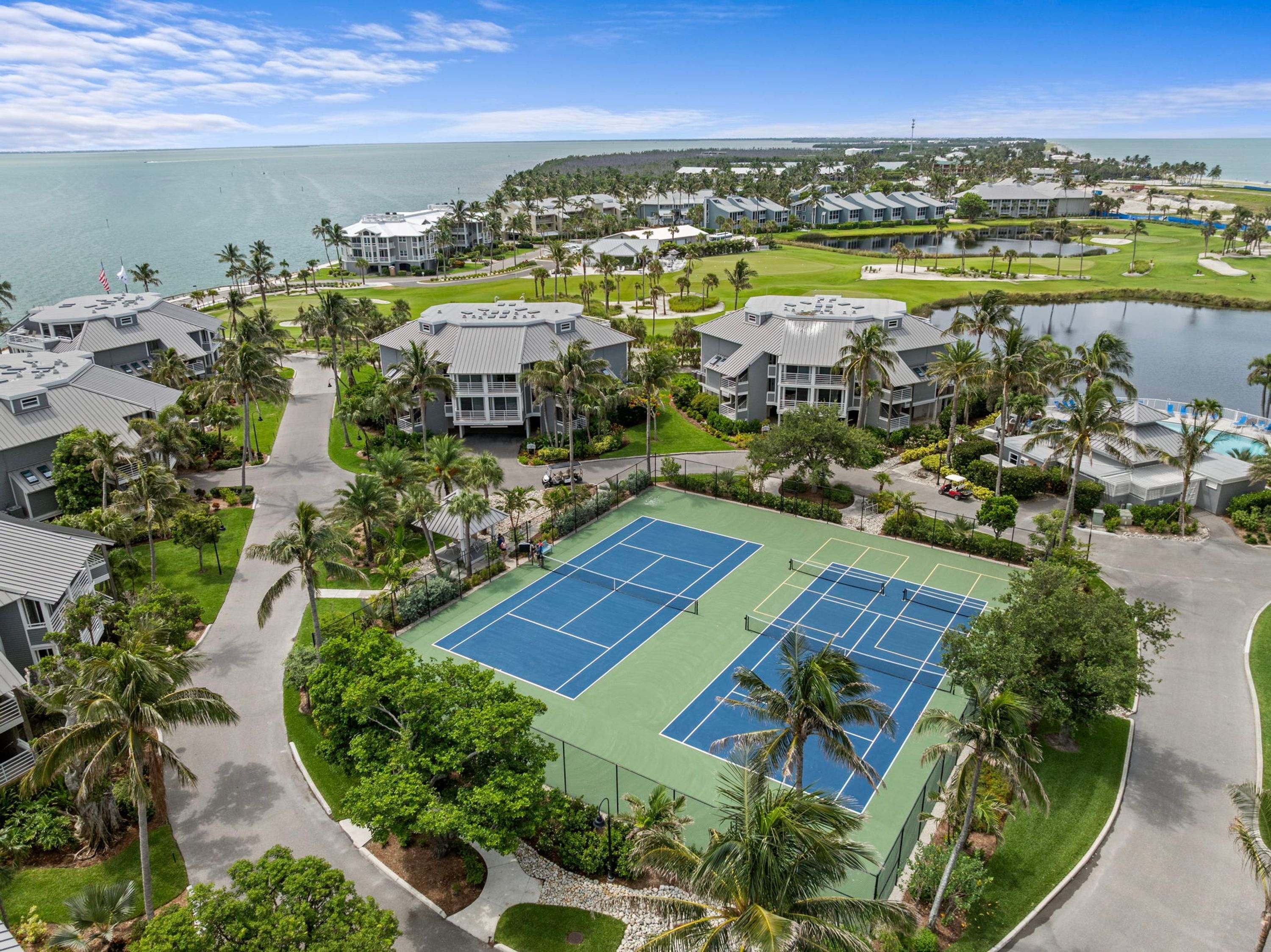 A resort with multiple buildings, a tennis court, and a view of the ocean.