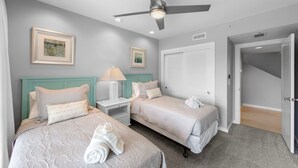 A hotel room with two beds, a ceiling fan, and artwork on the walls.