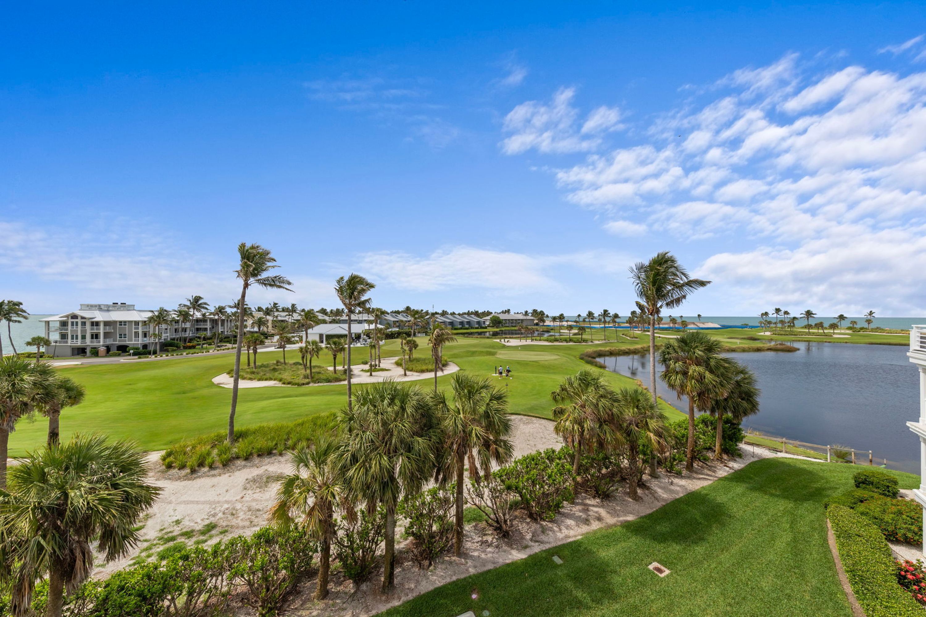 A golf course with a water body, palm trees, and a building in the background.