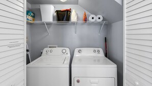 A laundry room with two washing machines, a shelf with cleaning supplies, and a water shutoff label.