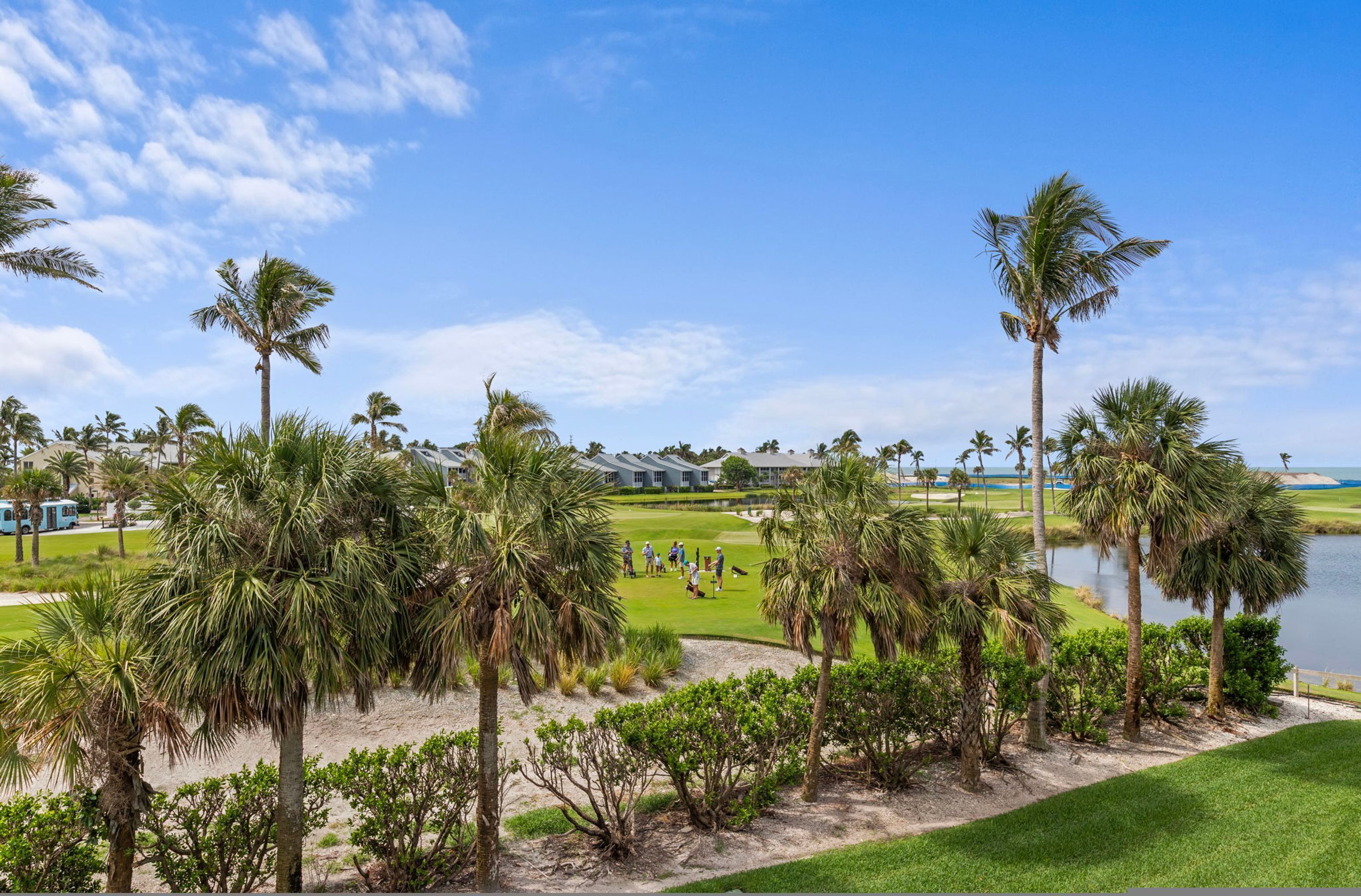 A golf course with a water body, palm trees, and a clubhouse.