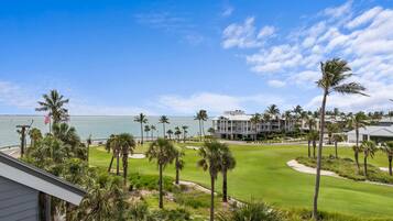Um campo de golfe com vista para o oceano e um edifício de resort com vários andares e varandas.