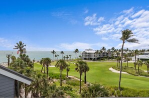 A golf course with a view of the ocean and a resort building with multiple floors and balconies.