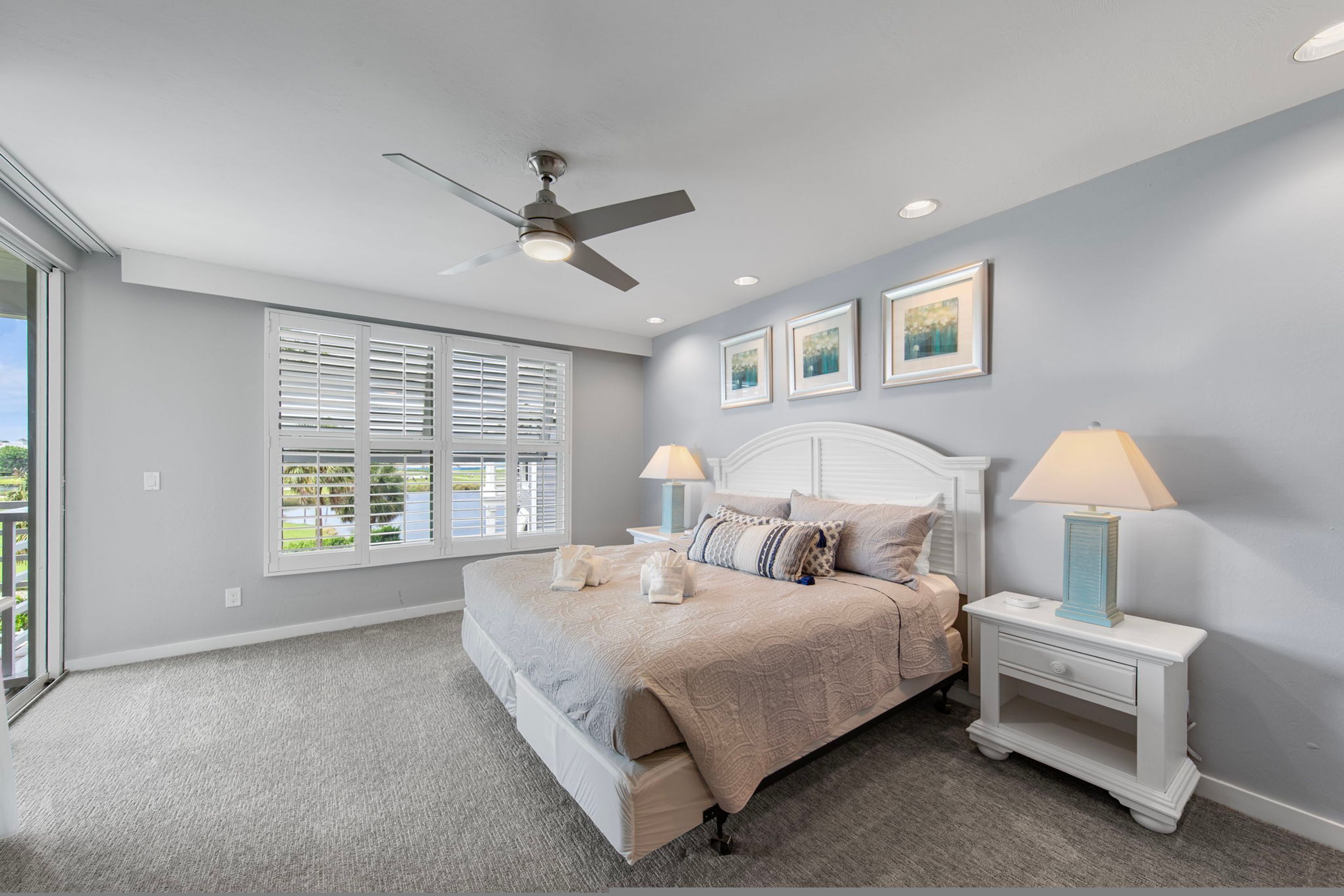 A bedroom with a bed, two bedside tables, a ceiling fan, and a window with blinds.