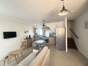 A modern kitchen with a dining area, a sofa, and a TV mounted on the wall. - L'Olivier - elegant gîte with terrace (Chailles)