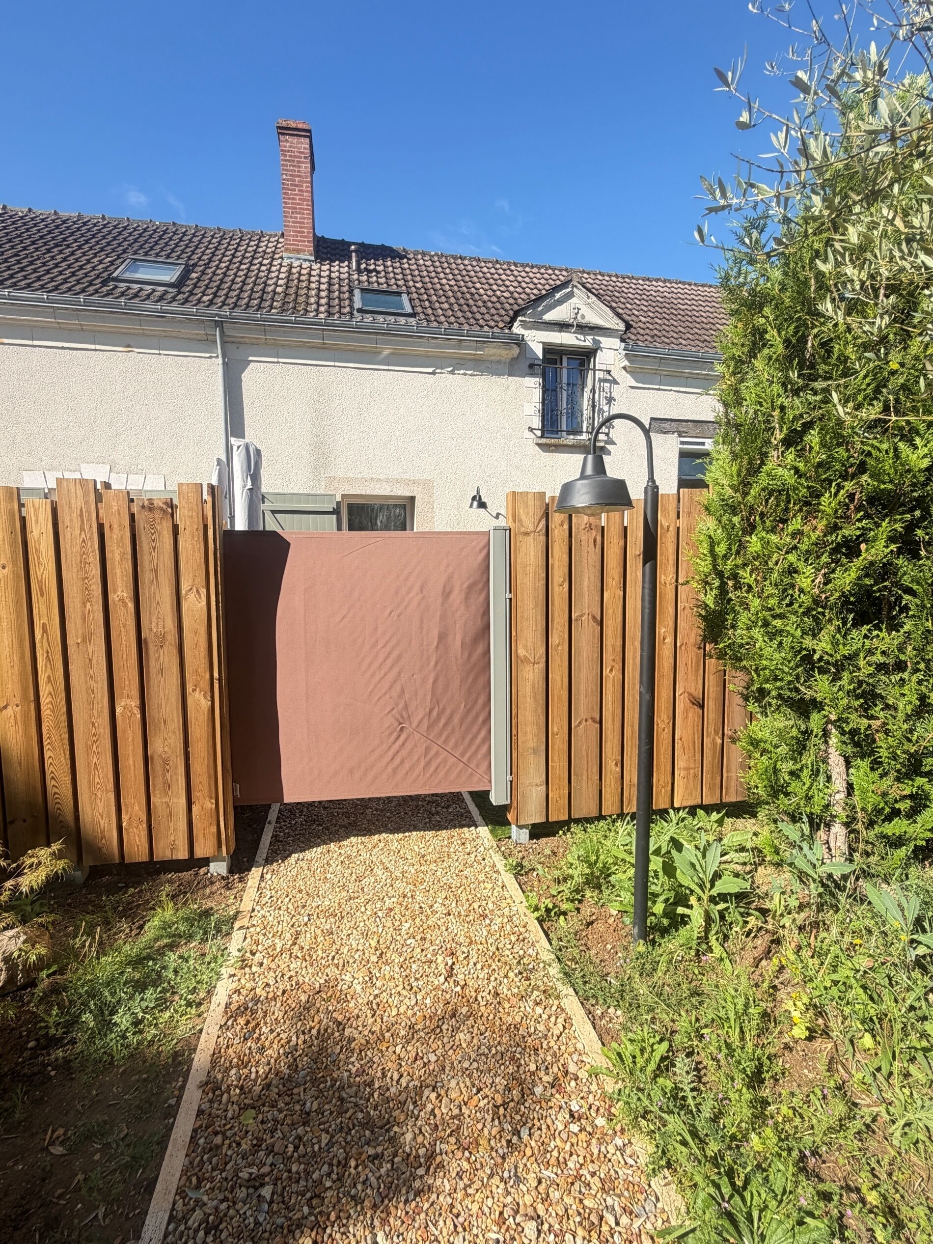 A house with a tiled roof, a wooden fence, a gravel pathway, and a small garden.