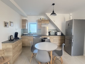 A modern kitchen with a dining area, featuring a stainless steel refrigerator, a coffee maker, and a window providing natural light. - L'Olivier - elegant gîte with terrace (Chailles)
