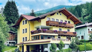 A multi-story hotel with balconies, a parking area, and a mountainous backdrop. - Room Josefine - Comfort room with mountain view, Julius Appartements Wagrain (Hofmark)