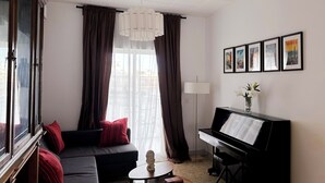 Ein Wohnzimmer mit einer Couch, einem Klavier, einer Lampe und einem Fenster mit Vorhängen.