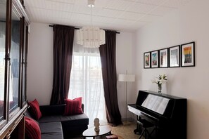Ein Wohnzimmer mit einer Couch, einem Klavier, einer Lampe und einem Fenster mit Vorhängen.