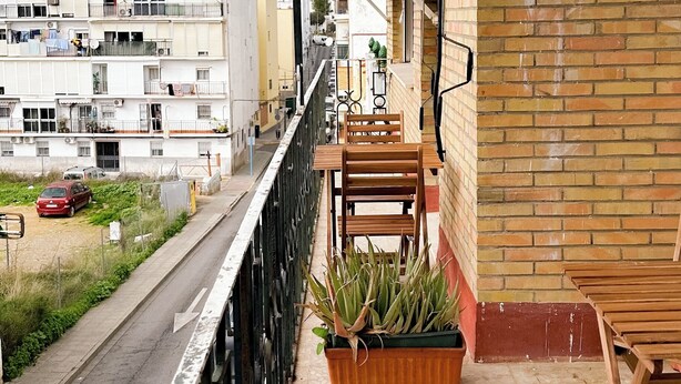 Ein Balkon mit Holzmöbeln, einer Topfpflanze und Blick auf eine Straße und Gebäude.