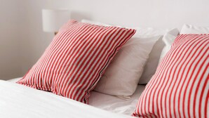 Ein Bett mit weißer Bettwäsche und zwei roten Kissen mit Streifen.
