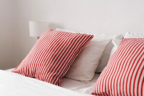 Ein Bett mit weißer Bettwäsche und zwei roten Kissen mit Streifen.