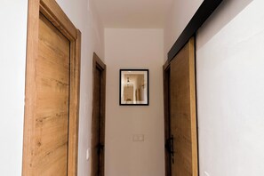 Ein schmaler Korridor mit Holztüren an beiden Seiten und einem gerahmten Bild an der Wand.