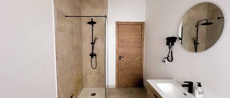 A modern bathroom with a glass-enclosed shower, a wooden door, a white sink with a black faucet, and a round mirror.