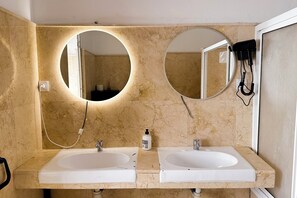Ein Badezimmer mit zwei Waschbecken, zwei Spiegeln und einem an der Wand montierten Föhn.