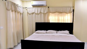 Ein Schlafzimmer mit schwarzem Kopfteil, einem Bett mit weißer Bettwäsche und beigen Vorhängen.