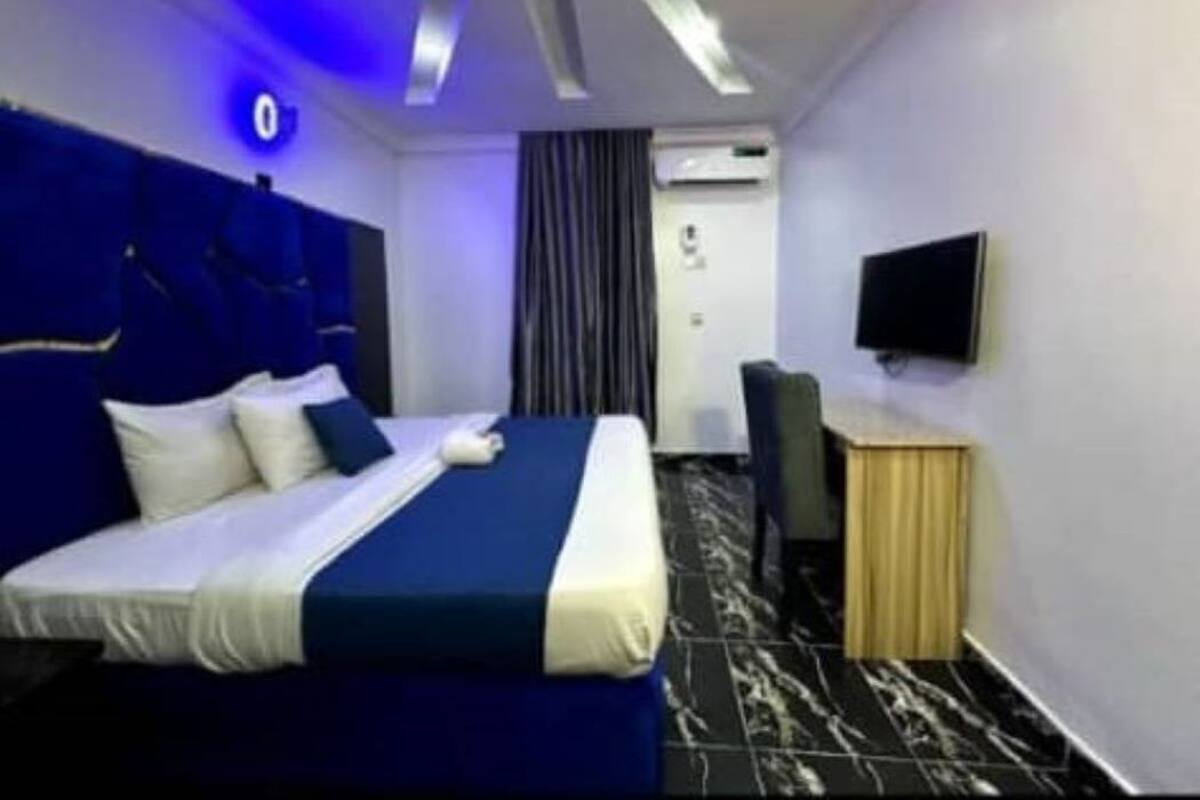 A hotel room with a bed, a desk, a chair, a flat-screen TV, an air conditioning unit, and a curtain.