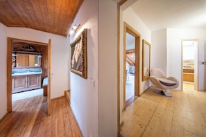 A hallway with wooden flooring, a framed picture on the wall, and a chair in the adjacent room.