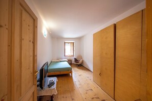 A bedroom with a wooden wardrobe, a bed, a chair, and a small table.