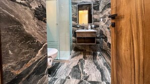 Ein Badezimmer mit Marmorwand, Duschkabine aus Glas, Holzwaschtisch und Spiegel.