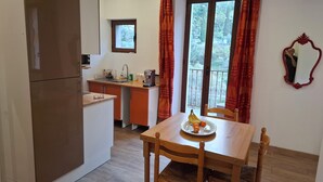 A compact kitchen with a dining area, a small window, and a balcony view. - Furnished Appartment Au Pied du Mercantour (Fontan)