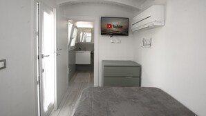 Een slaapkamer met een bed, een aan de muur bevestigde televisie, een klein bureau en een deur naar een badkamer.