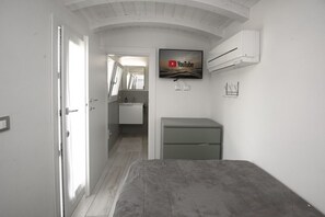 Ein Schlafzimmer mit Bett, einem an der Wand befestigten Fernseher, einem kleinen Schreibtisch und einer Tür zu einem Badezimmer.
