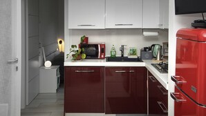 Een kleine keuken met witte bovenkastjes, een rode koelkast en een magnetron op het aanrecht.