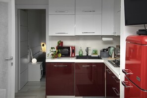 Eine kleine Küche mit weißen Oberschränken, einem roten Kühlschrank und einer Mikrowelle auf der Arbeitsplatte.