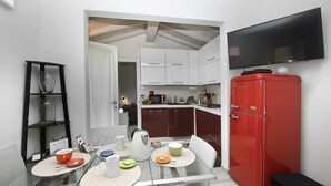 Een moderne keuken met witte kasten, een rode koelkast, een glazen eettafel en een flatscreen televisie aan de muur.