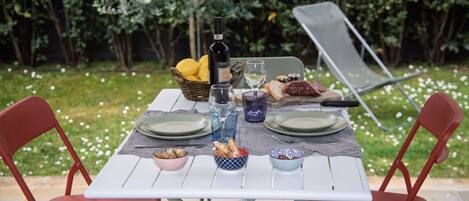 A table set outdoors with a bottle, glasses, bread, and bowls.